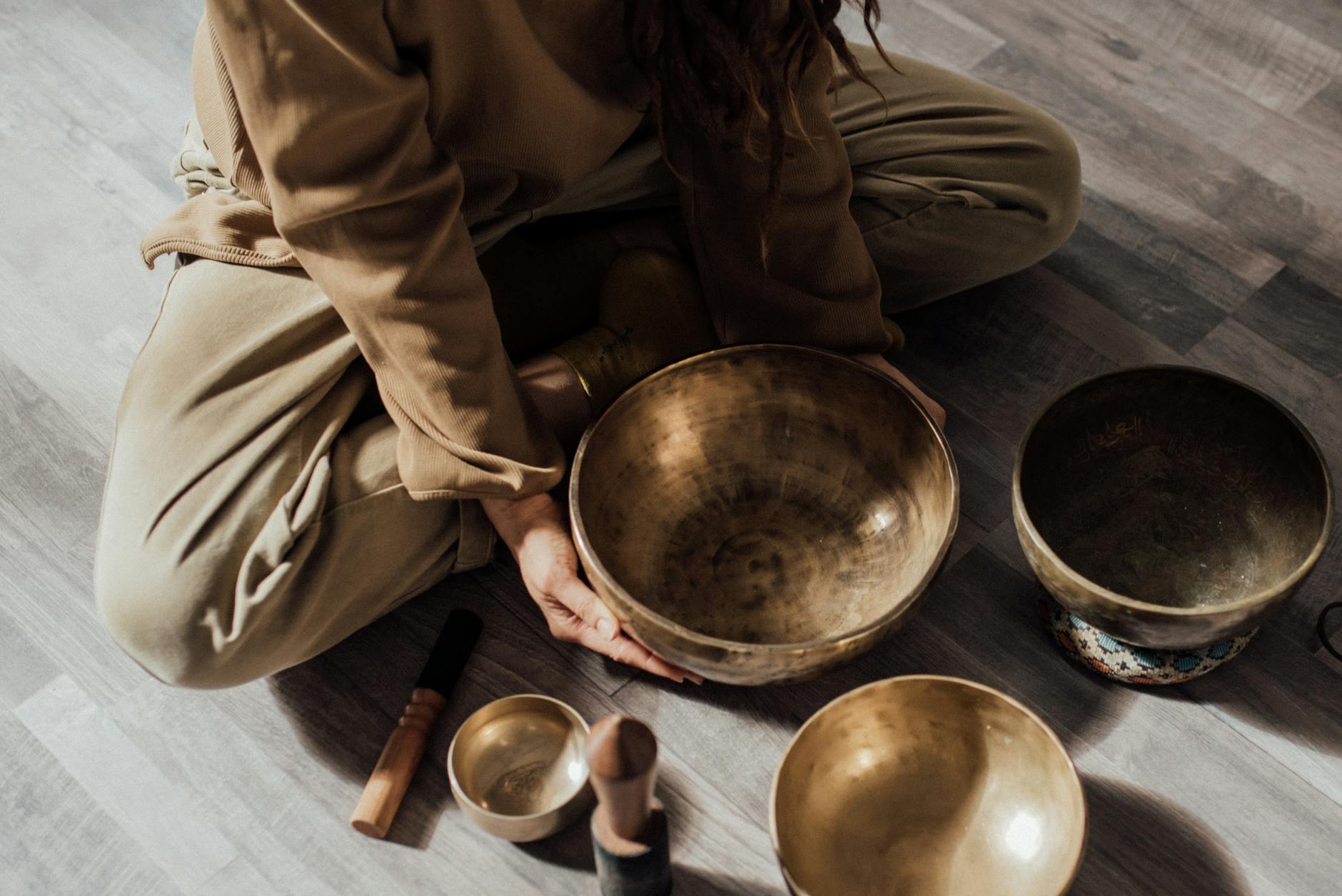 a person sitting on the floor with metallic bowls, evoking advanced meditation techniques, deep meditation practice, meditation journey, advanced mindfulness, and spiritual growth meditation