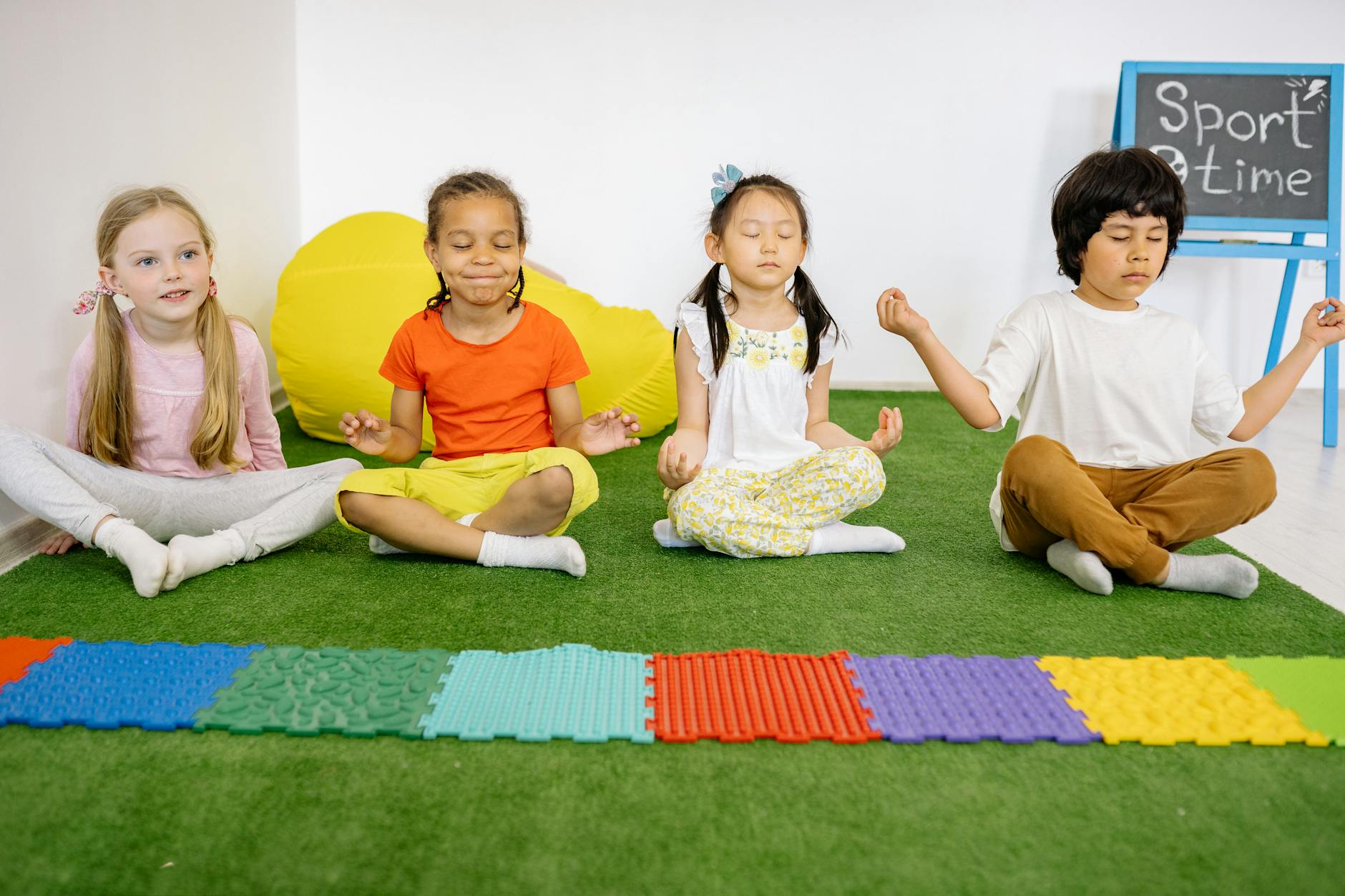 children sitting on green mat in yoga position, showing the importance of interconnectedness, meditation, oneness, unity and compassion, and connection with nature
