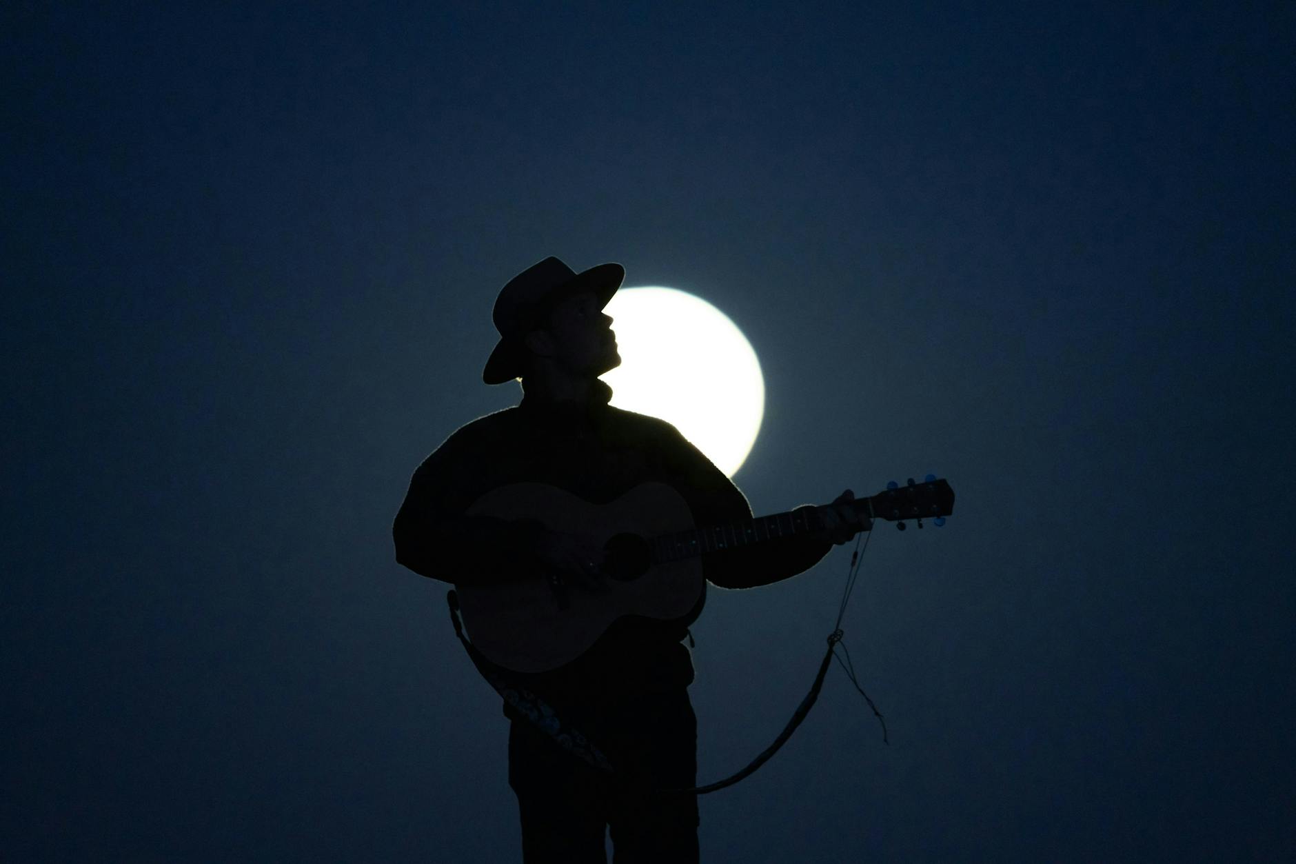 man playing acoustic guitar under moon, illustrating lunar cycle, moon rituals, moon phases meaning, lunar wisdom, and working with the moon