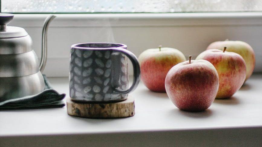 a mug cup beside the wet glass window, illustrating: how to Celebrate Mabon, spiced apple cider recipe, autumn ritual, seasonal drink, and the Wheel of the Year