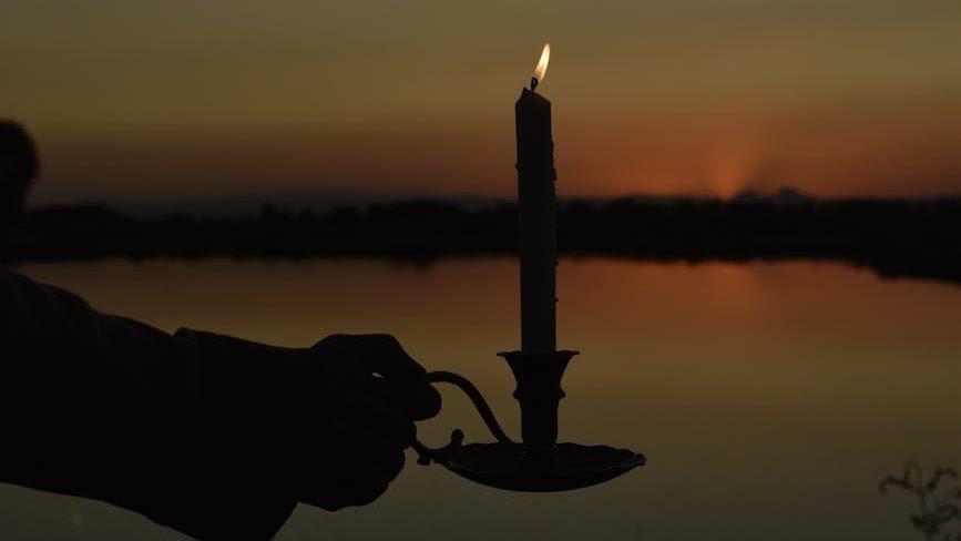 silhouette of a person holding a lit candle on the background of a lake at sunset